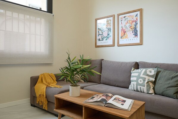 A living room with a grey sofa, a wooden coffee table with a magazine, a yellow throw blanket, a potted plant, and two framed artworks on the wall. - Casa Cosi - Don Bajos (Barcelona)