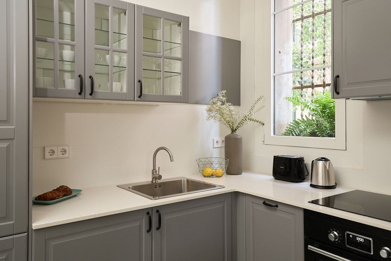 A modern kitchen with grey cabinets, a stainless steel sink, a toaster, and a kettle.