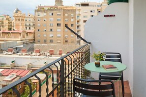 Een balkon met een tafel en stoelen, met uitzicht op een stadsgezicht met diverse gebouwen.