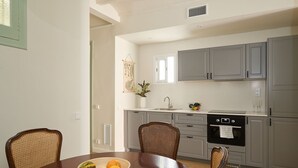 A dining area with a round table, two chairs, and a bowl of fruit. The kitchen in the background has grey cabinets, a sink, and an oven. - Casa Cosi - El Farro 4 (Barcelona)