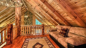 Acogedor dormitorio en el ático, con techo de madera, pared de piedra, baranda de madera, un sofá y una alfombra estampada.
