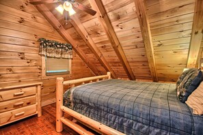 Un dormitorio de cabaña de madera con cama, cómoda y ventana con cortinas.