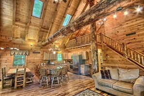 A wooden cabin interior with a dining area, kitchen, and a staircase leading to a loft.