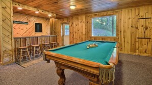 Una mesa de billar en una sala con paredes de madera y una zona de bar.