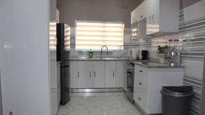 A modern kitchen with white cabinets, a stainless steel refrigerator, a sink with a faucet, and a trash bin. - Escape Go Nest (Harare)