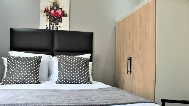A bed with a black headboard, white and grey polka dot pillows, and a grey blanket. - Escape Go Nest (Harare)