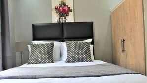 A neatly made bed with a black headboard, white and polka-dotted pillows, and a gray blanket. - Escape Go Nest (Harare)