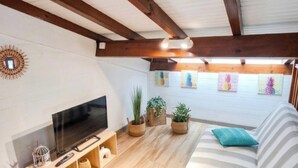 Un salón con televisión, vigas de madera, paredes blancas y plantas en macetas.