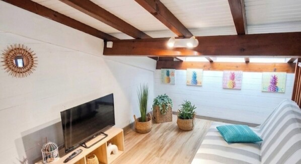 Un salon avec un téléviseur, des poutres en bois, des murs blancs et des plantes en pot.