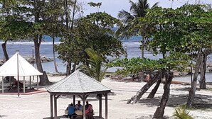 Escena de playa con un pabellón, palmeras y vistas al océano.
