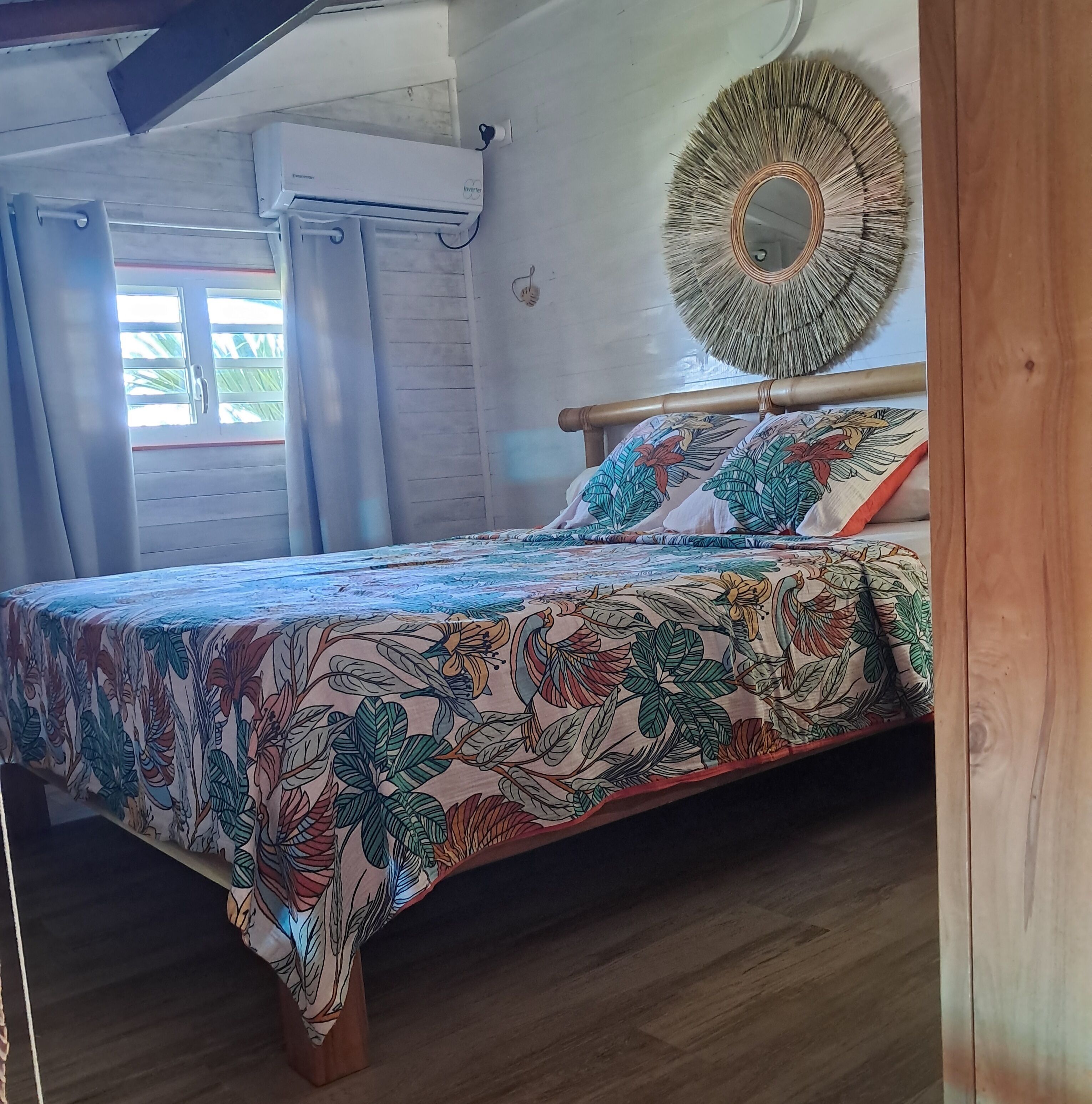 Een slaapkamer met een bed, gordijnen, een wandspiegel en een raam met gordijnen.
