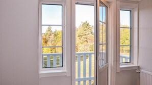 Una habitación con tres ventanas, cada una con marco blanco y vistas a una terraza de madera y árboles.