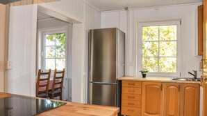 Una cocina con armarios de madera, un refrigerador de acero inoxidable, un ventanal con vista a árboles y una zona de comedor con mesa y sillas.