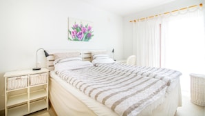 Ein Schlafzimmer mit Bett, Nachttischen, einer Lampe, einem Gemälde und einem Fenster mit Vorhängen.