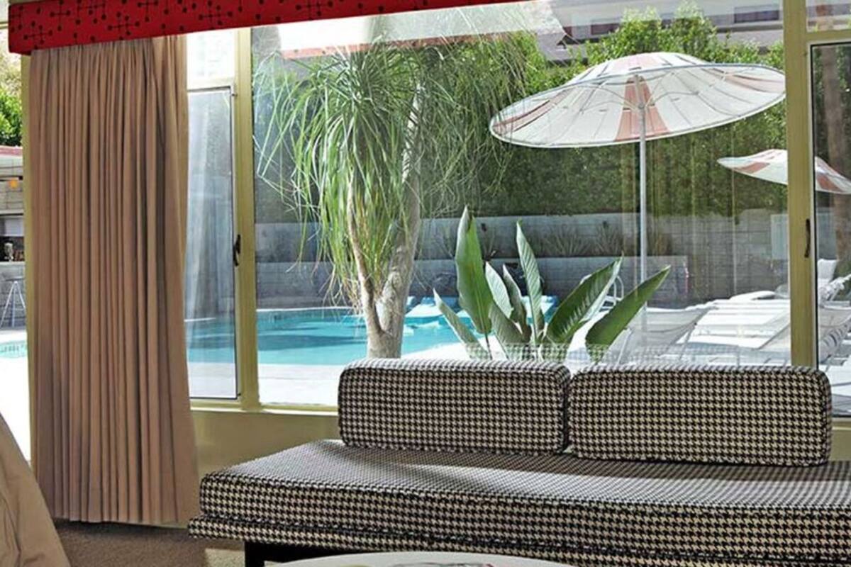 A hotel room with a large window, a sofa, and a view of a pool and umbrellas outside.