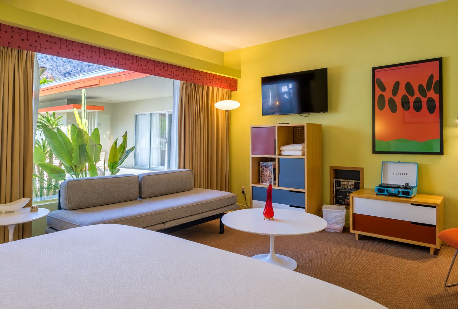 Et hotelværelse med en seng, en sofa, et fjernsyn, et lille bord og en bogreol.