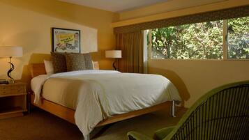 A hotel room with a bed, bedside lamps, a nightstand, a chair, and a window with a view of trees.