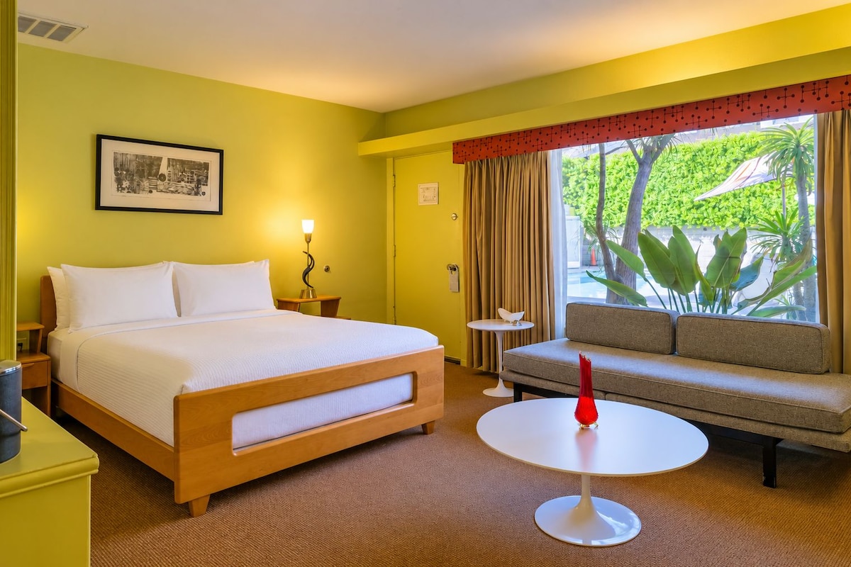 Una habitación de hotel con cama, sofá, una mesita y ventana con cortinas.