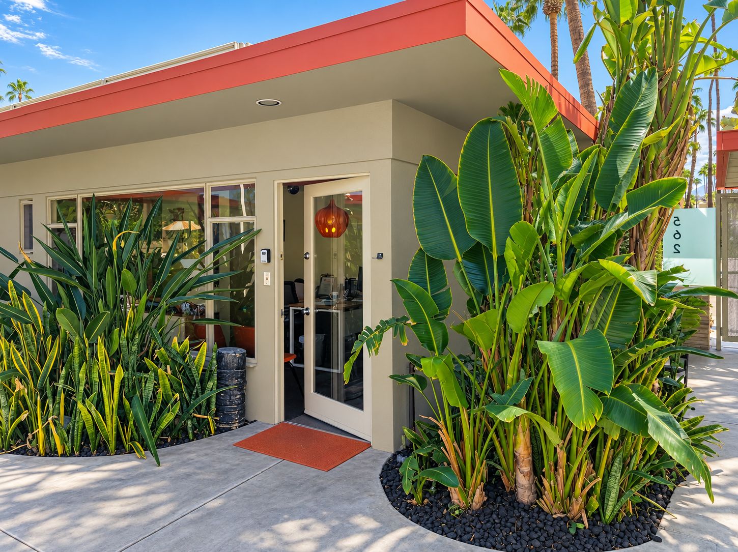 A building with a red roof and a glass door entrance, surrounded by tropical plants.