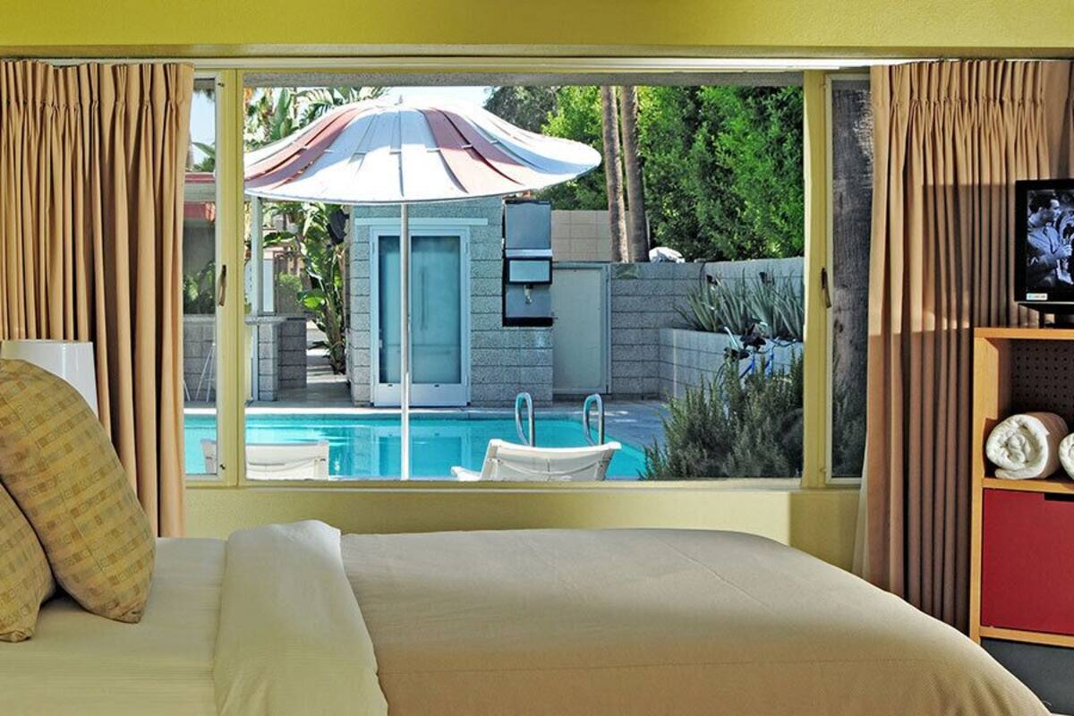 A hotel room with a bed, a TV, and a view of an outdoor swimming pool.