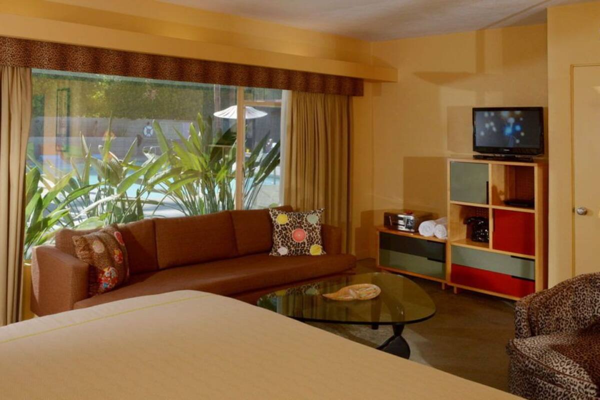 A hotel room with a large bed, a sofa, a glass coffee table, a television, and a wardrobe.