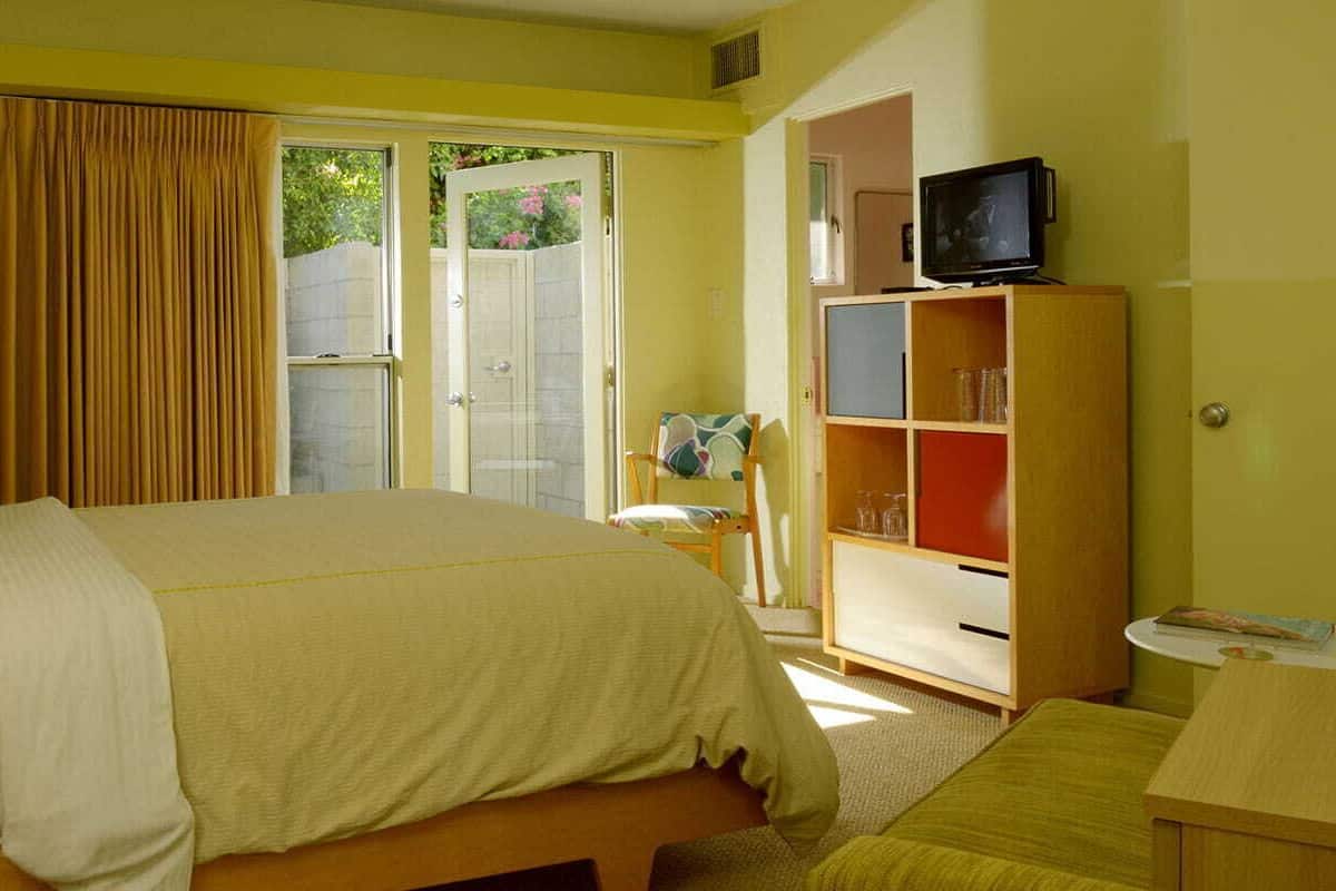 A hotel room with a bed, a television, a bookshelf, and a desk.