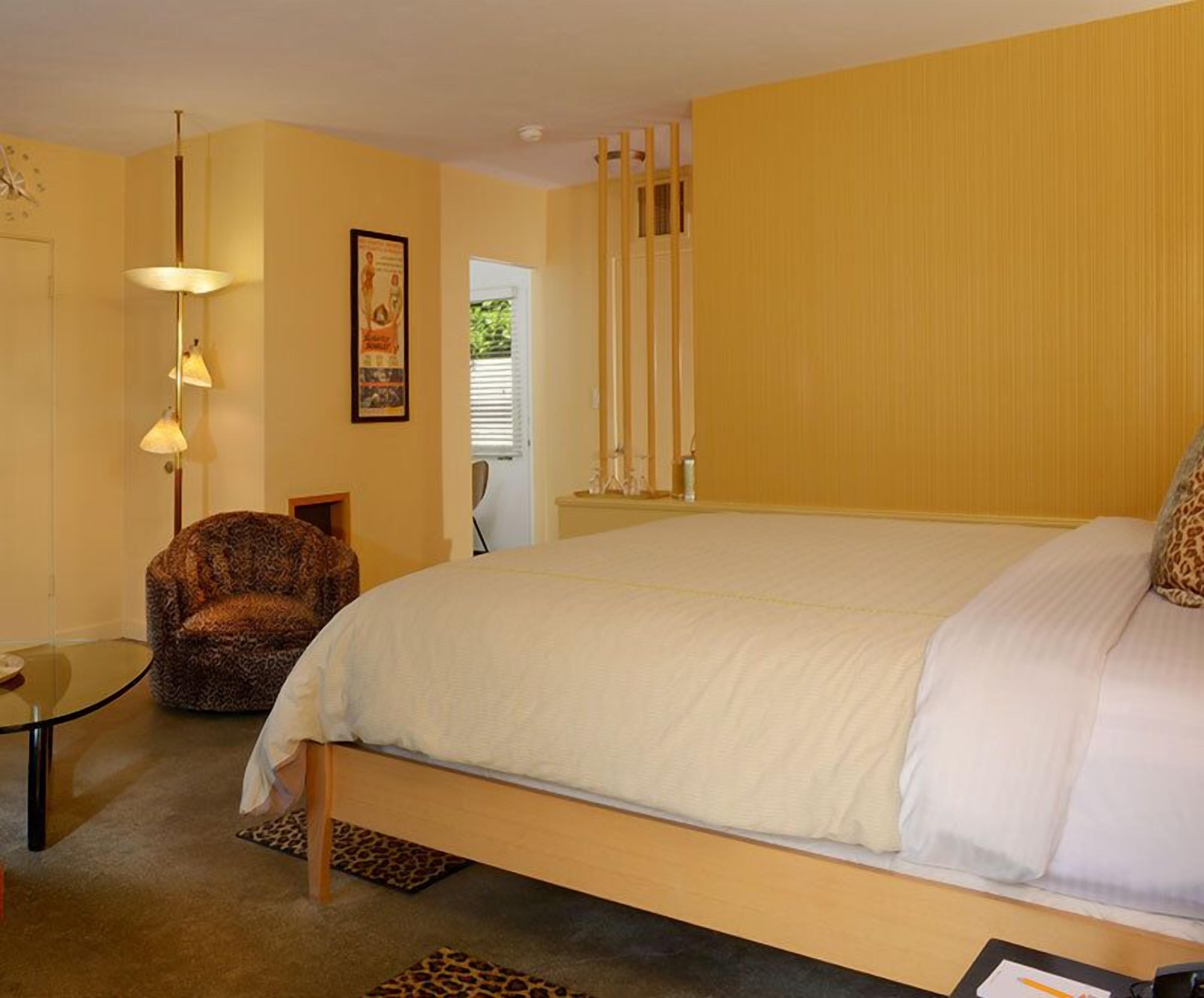 Un dormitorio con una cama grande, una silla, una mesita y una puerta que da a otra habitación.