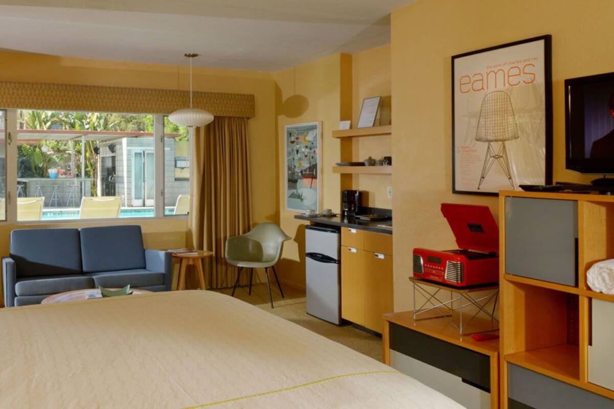 A hotel room with a bed, a sofa, a desk, a chair, a television, and a window with curtains.