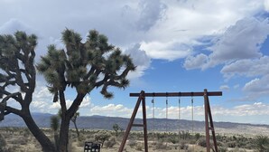 A desert landscape with a large Joshua tree, a wooden swing set, and a bench.