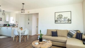 A modern living room with a sofa, a dining area with chairs, a coffee table, and a kitchen in the background.