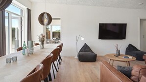 A modern living room with a dining area, a flat-screen TV, and a large window. - Stunning home in Blokhus with kitchen (Blokhus)