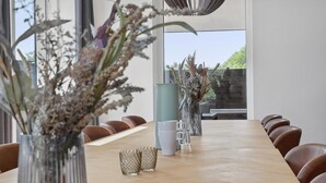 A long wooden table with six brown leather chairs, flanked by large windows and indoor plants. - Stunning home in Blokhus with kitchen (Blokhus)