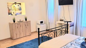 A bedroom with a bed, a TV, a dresser, a microwave, and a painting on the wall.