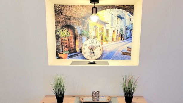 A wooden cabinet with two potted plants, a decorative tray, and a framed picture of a street scene with a clock.