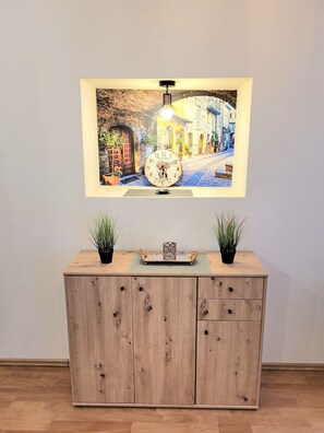 A wooden cabinet with two potted plants, a framed picture of a street scene, and a clock. - Near train station&Old City, renovated (Kraków)