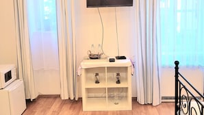 A room with a flat-screen TV mounted on the wall, a white console table with decorative items, a blue rug, and a bed with a black metal frame.