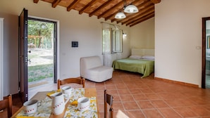 A room with a dining table set with white cups and a pitcher, a white chair, a bed with a green bedspread, and a wooden ceiling. - Gorgeous home in Giove (Giove)