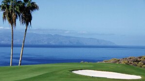 Ein Golfplatz mit freiem Blick auf das Meer und Berge im Hintergrund.