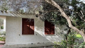 Un edificio rustico con due finestre, un vialetto in pietra e vegetazione circostante.