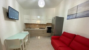 Una cucina compatta con un tavolo da pranzo, sedie, un divano rosso e una TV a schermo piatto montata a parete.