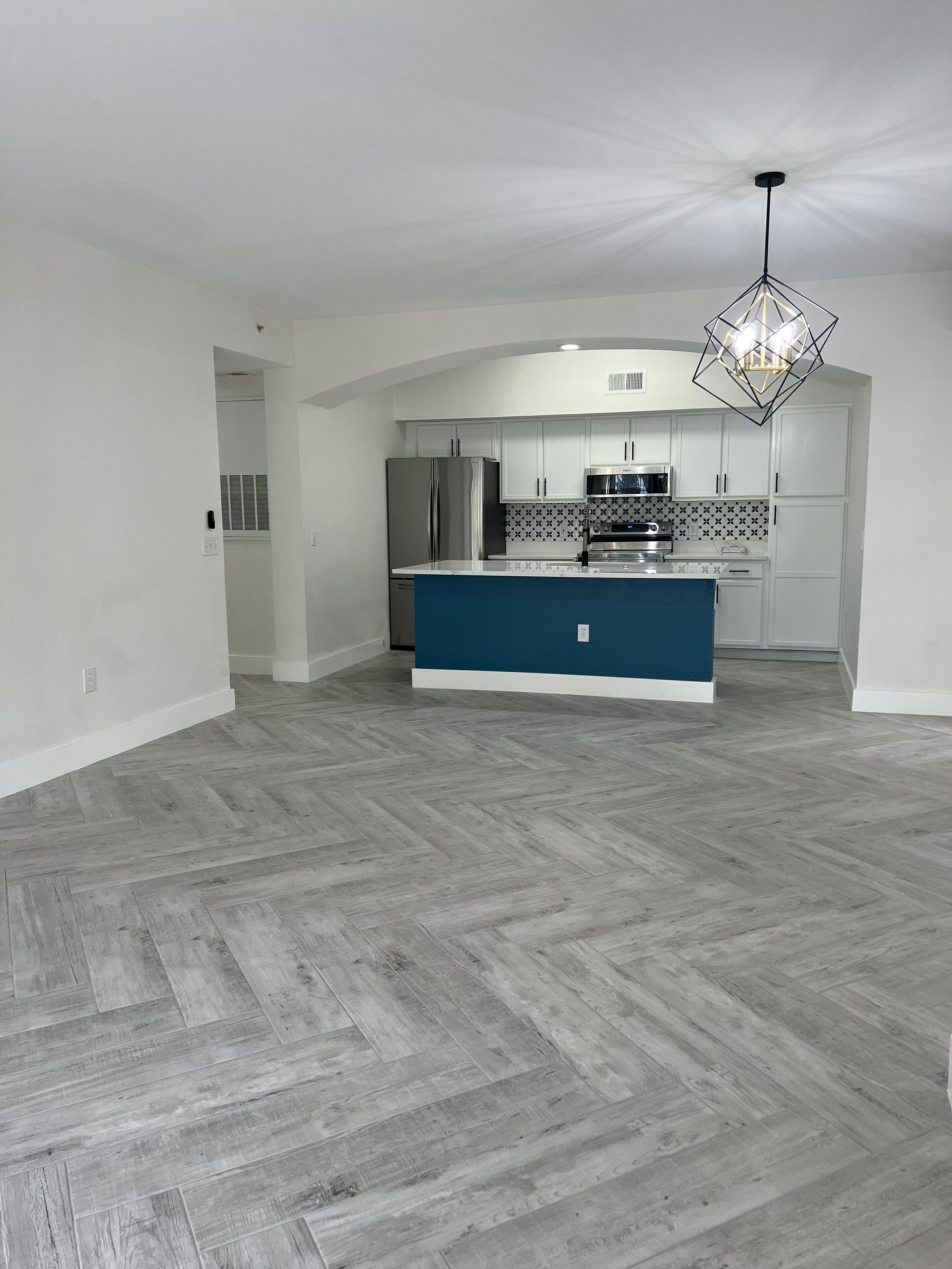 A spacious kitchen with white cabinets, a blue island, and a modern chandelier.