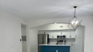 Une cuisine spacieuse avec des meubles blancs, un îlot central bleu et un lustre moderne.