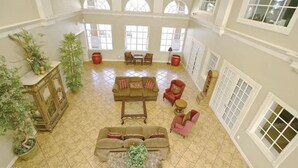 Un intérieur spacieux avec un plafond haut, de grandes fenêtres et un espace salon central agrémenté de canapés et de fauteuils.