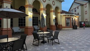 Un espace extérieur aménagé en terrasse, avec des tables et des chaises rondes, entouré d’arcades et de colonnes.