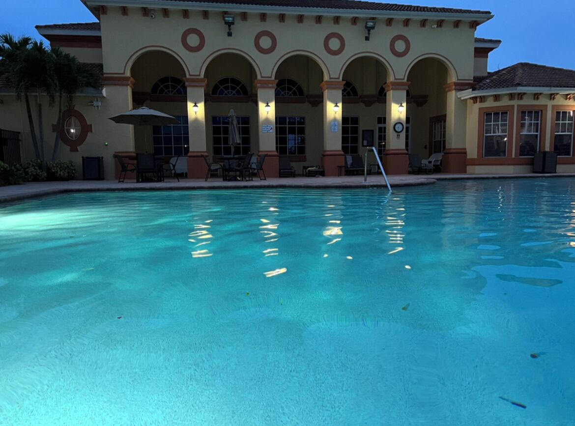A swimming pool with a building in the background featuring arched windows and outdoor seating.