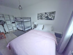 Un dormitorio con literas, una mesita de noche con lámpara, una obra de arte colgada en la pared y una ventana con cortinas.