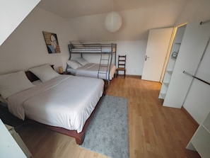 A dorm-style room with bunk beds, a wooden floor, a gray rug, a ladder, and a door.