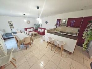 Eine moderne Wohnung mit Essbereich, einem roten Sofa, einer Küche mit Marmorarbeitsplatte und einem kleinen Balkon.