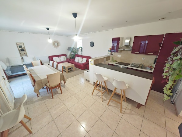 A modern apartment with a dining area, a red sofa, a kitchen with a marble countertop, and a small balcony.