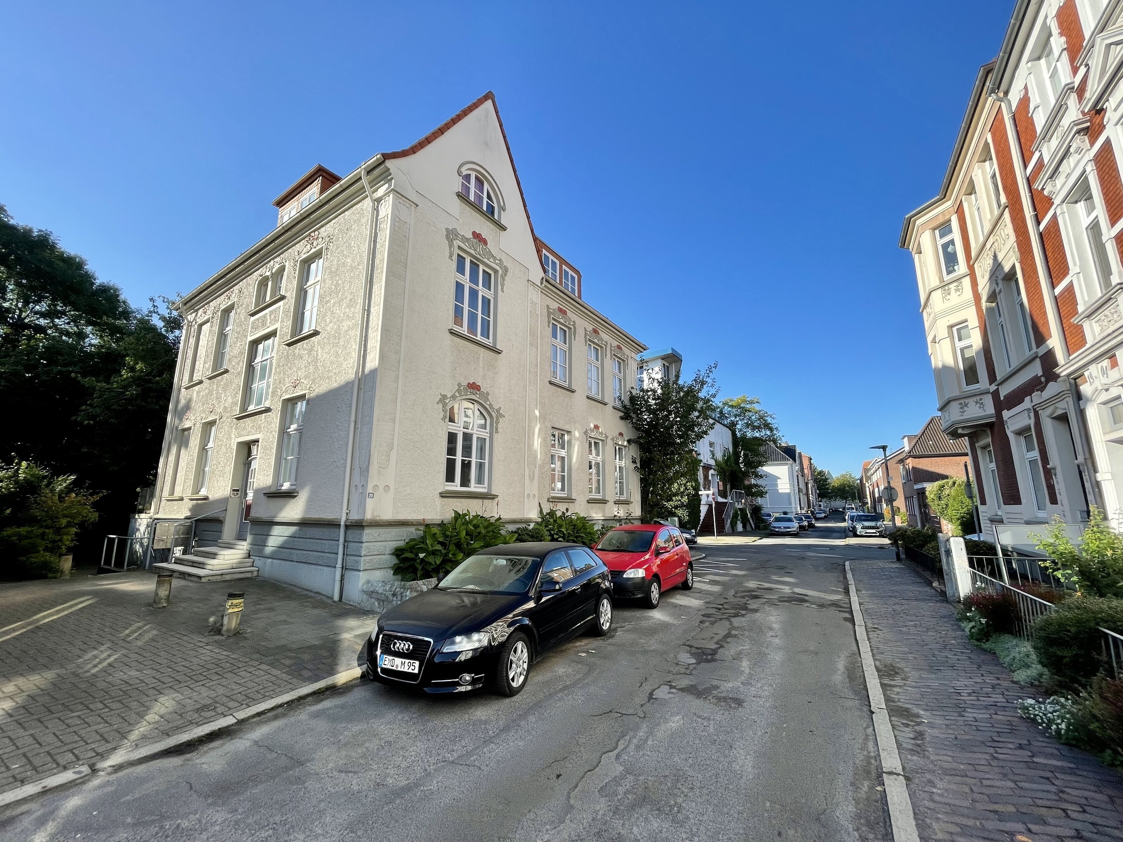 Straßenansicht eines zweistöckigen Gebäudes mit klassischer Architektur, dekorativen Elementen und einem roten Ziegeldach.